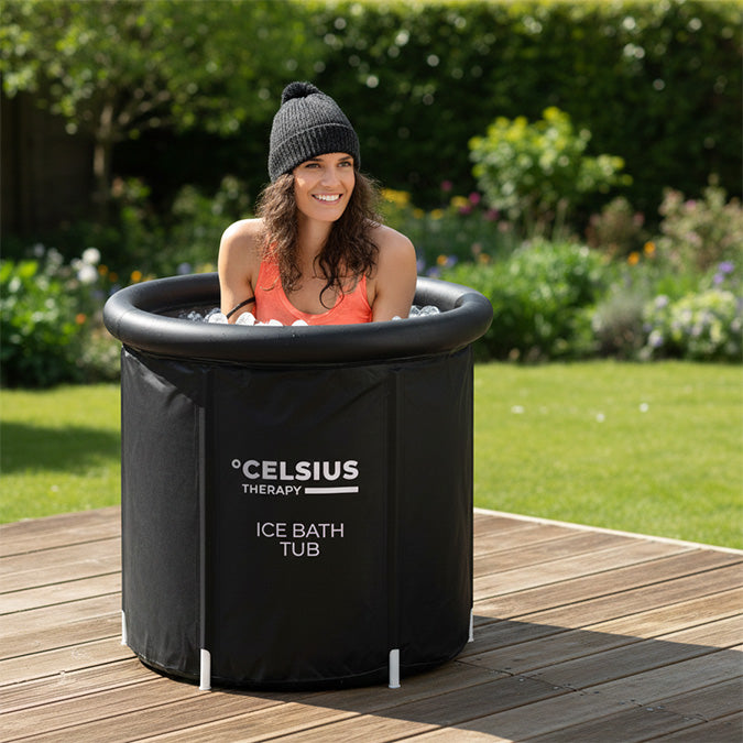 Woman in an ice bath tub outdoors on a wooden deck with greenery in the background